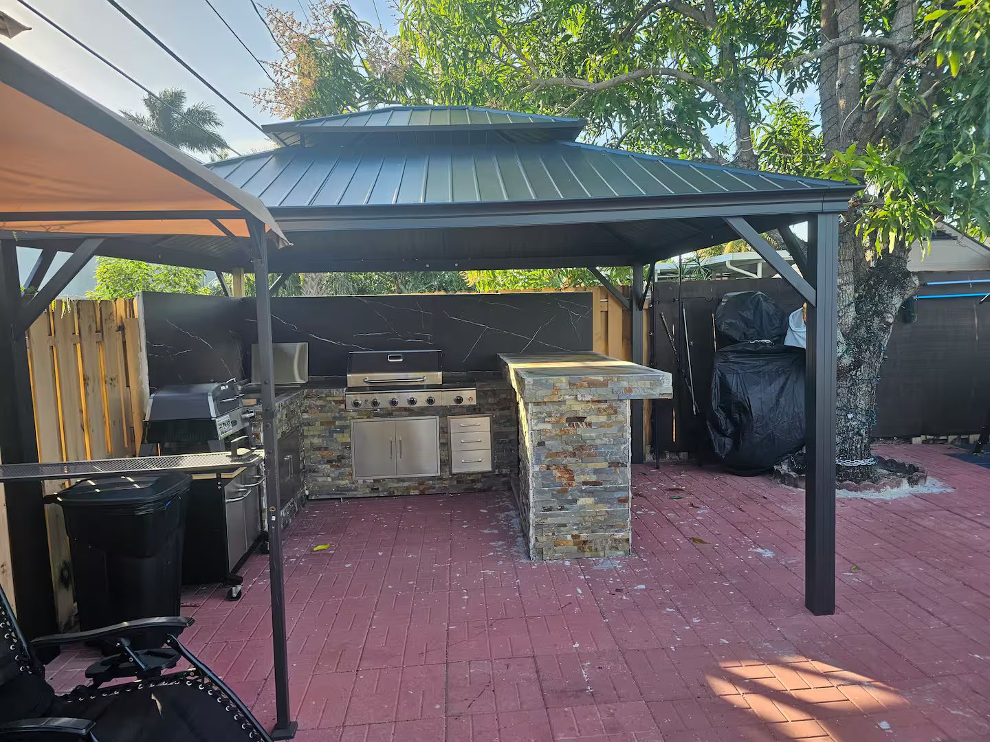 An outdoor kitchen area with a grill, a pizza oven, and a stone countertop.