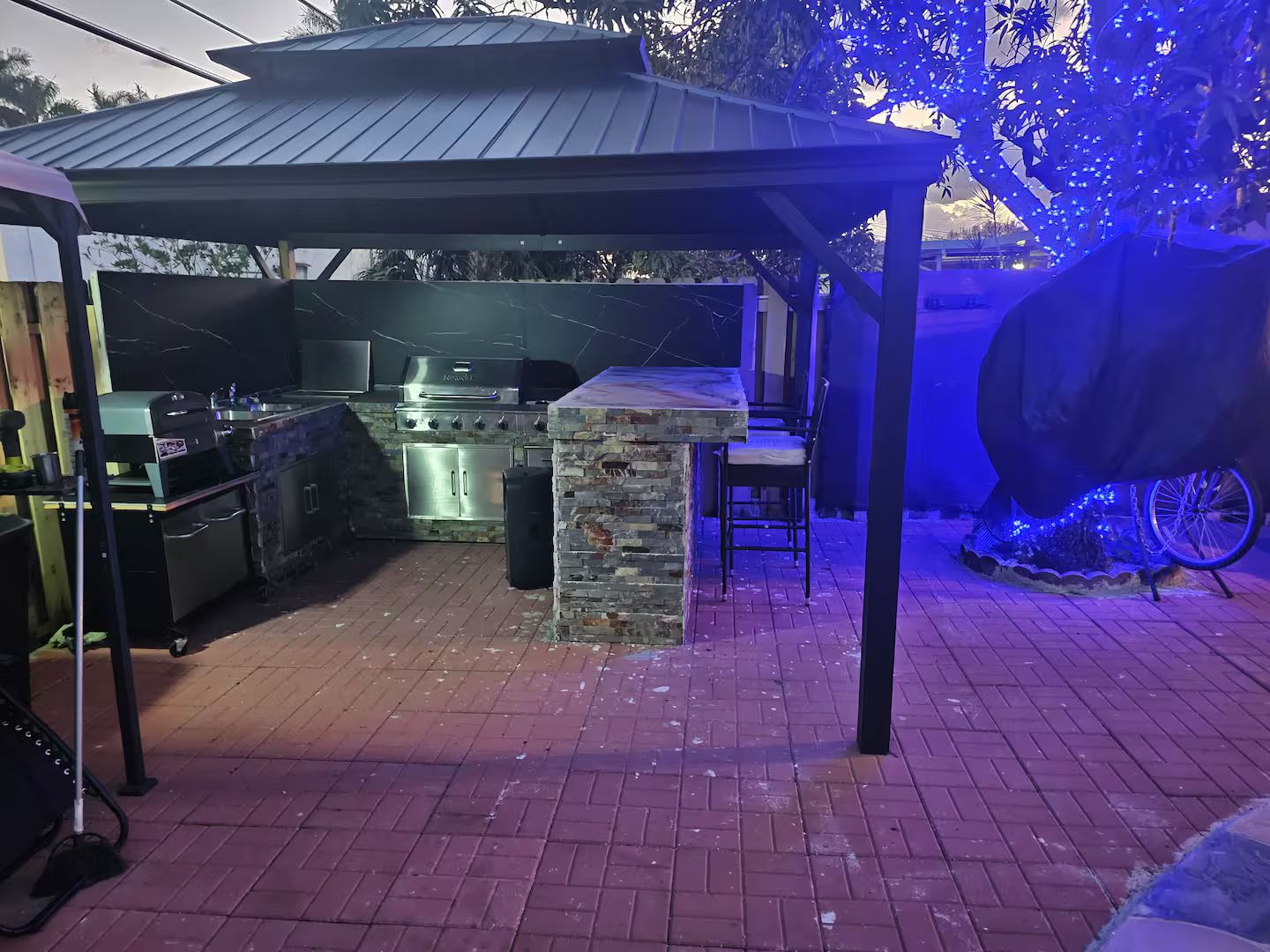 Ein Außenbereich mit Küche, inklusive Grill, Spüle und Arbeitsplatte aus Stein.