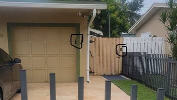 A residential garage with a car parked inside, a covered patio area, and a fenced backyard.