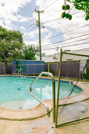 A swimming pool with a metal ladder and a covered area, surrounded by a fence and trees.