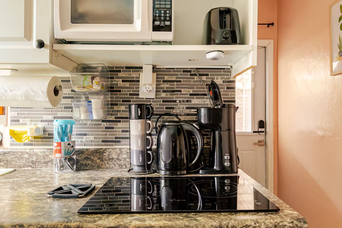 Una cocina con cafetera, hervidor y microondas sobre la encimera.
