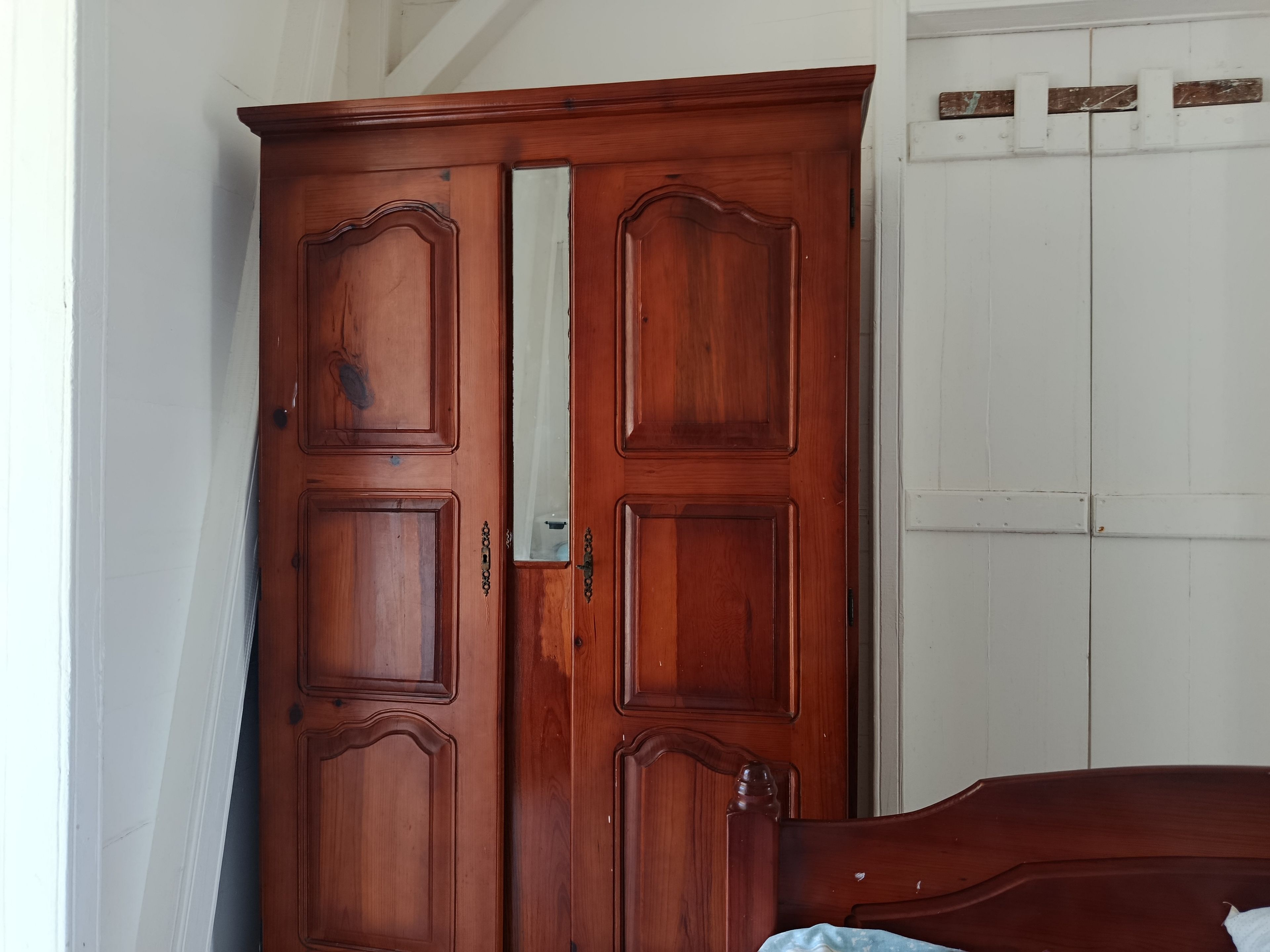 Une armoire en bois avec un miroir et un lit avec une tête de lit en bois.
