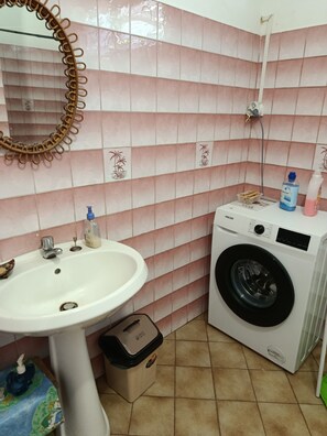Une salle de bain avec un lavabo, un miroir, un lave-linge et des murs carrelés.