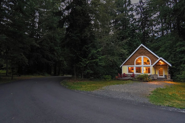 A two-story cabin with a curved driveway, surrounded by dense forest.