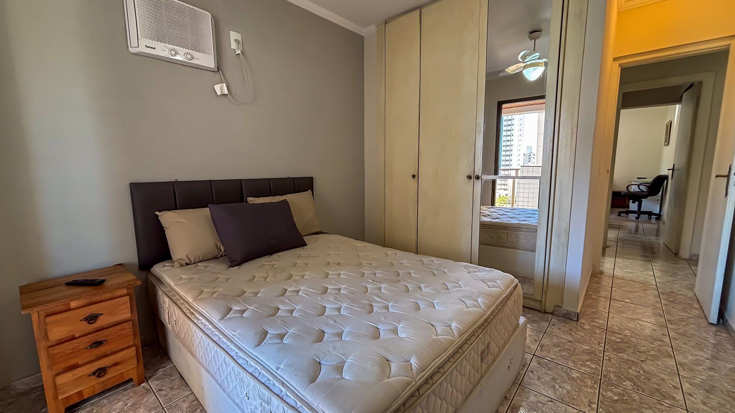 A bedroom with a bed, a wooden nightstand, a wardrobe, and a ceiling fan.
