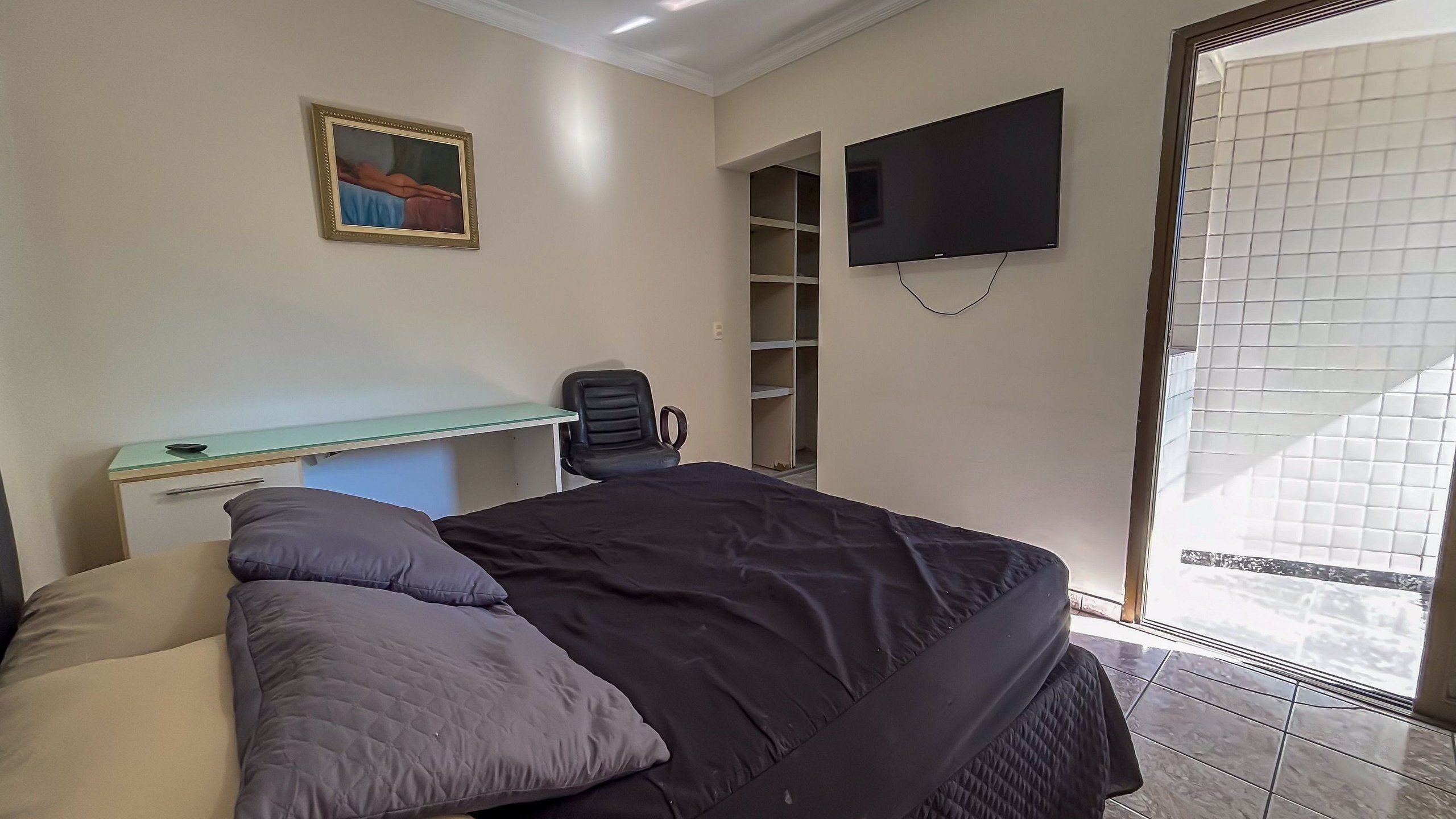 Un dormitorio con cama, escritorio, silla, televisor y ventana.