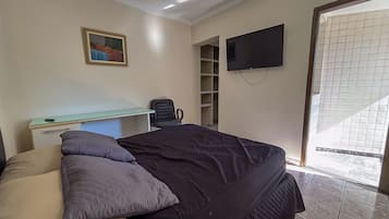 Un dormitorio con cama, escritorio, silla, televisor y ventana.