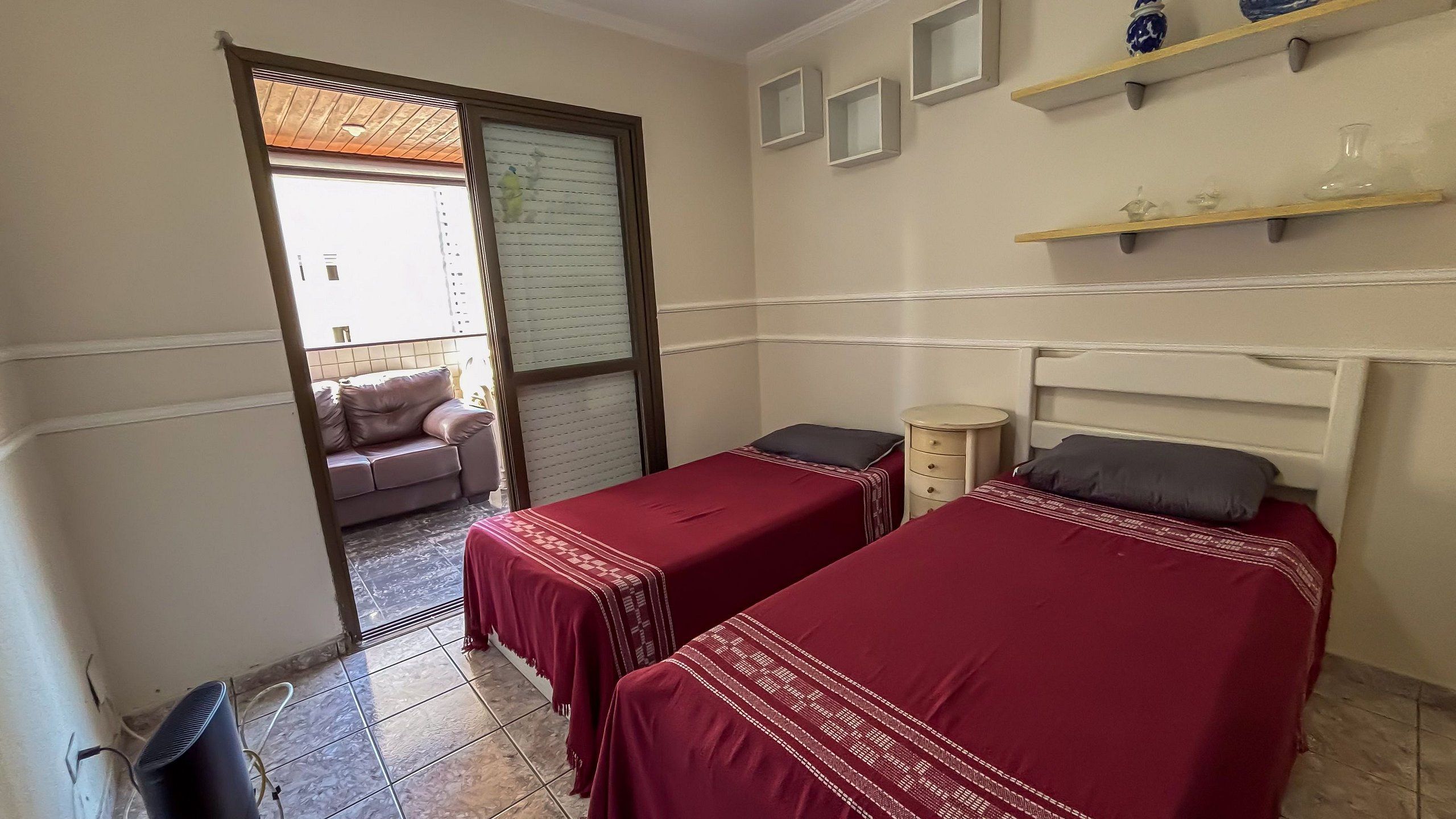 A bedroom with two single beds, a small bedside table, a chair, and a window with blinds.