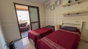 Un dormitorio con dos camas individuales, una mesita de noche pequeña, una silla y una ventana con persianas.