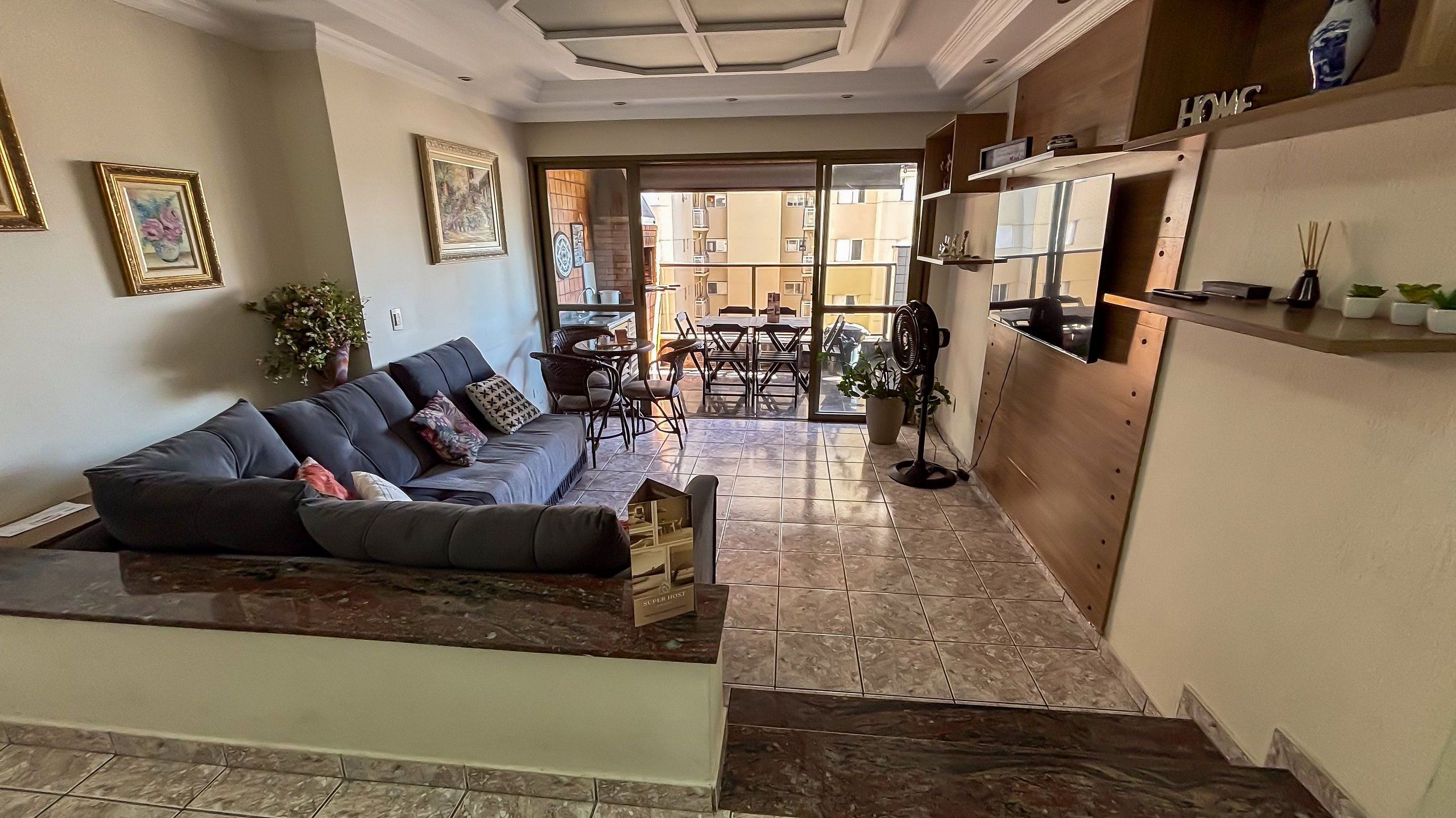 A living room with a sofa, a dining table, and chairs. There is a fan and a potted plant.