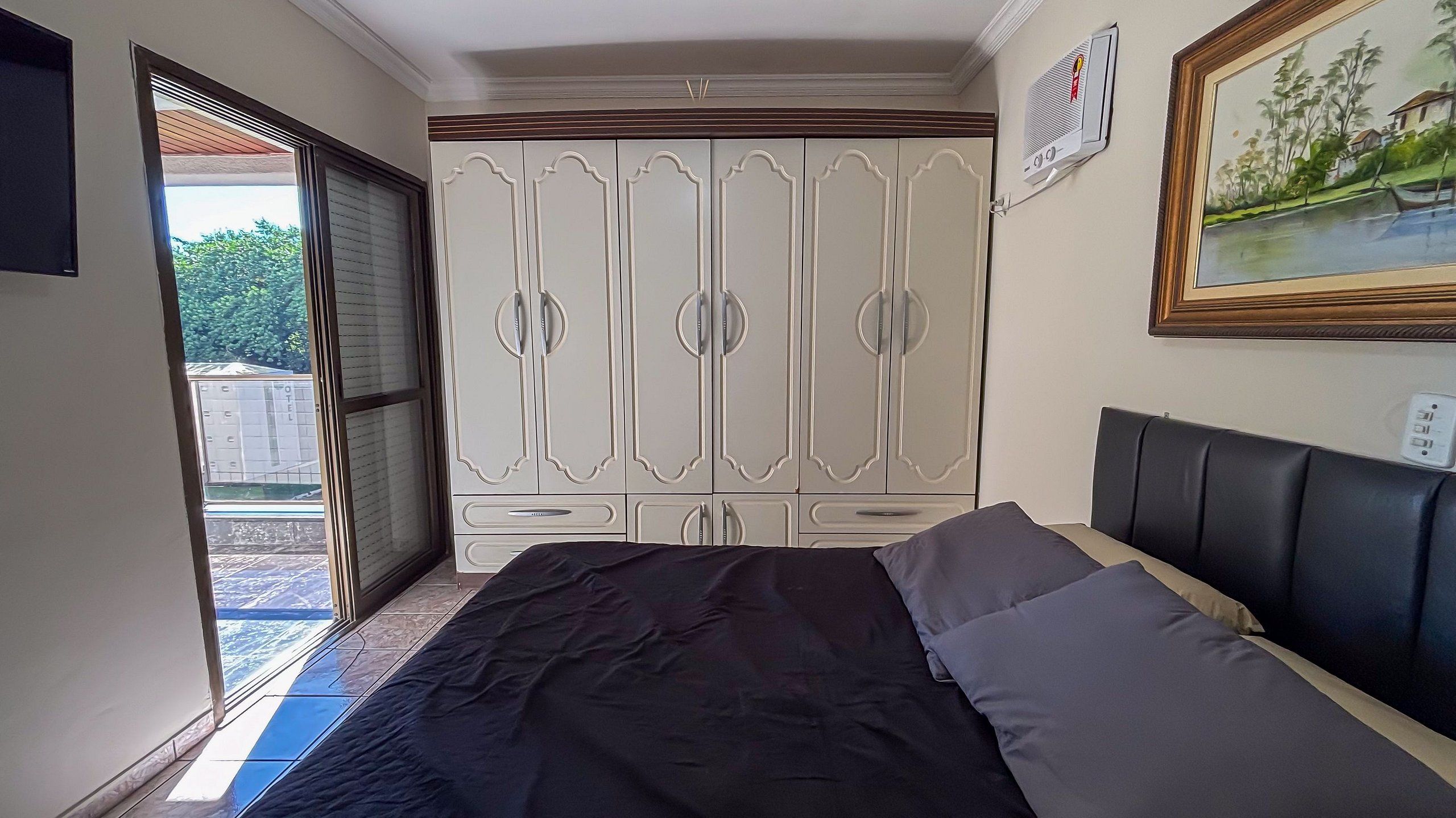 Een slaapkamer met een bed, een kast, een schilderij en een raam.