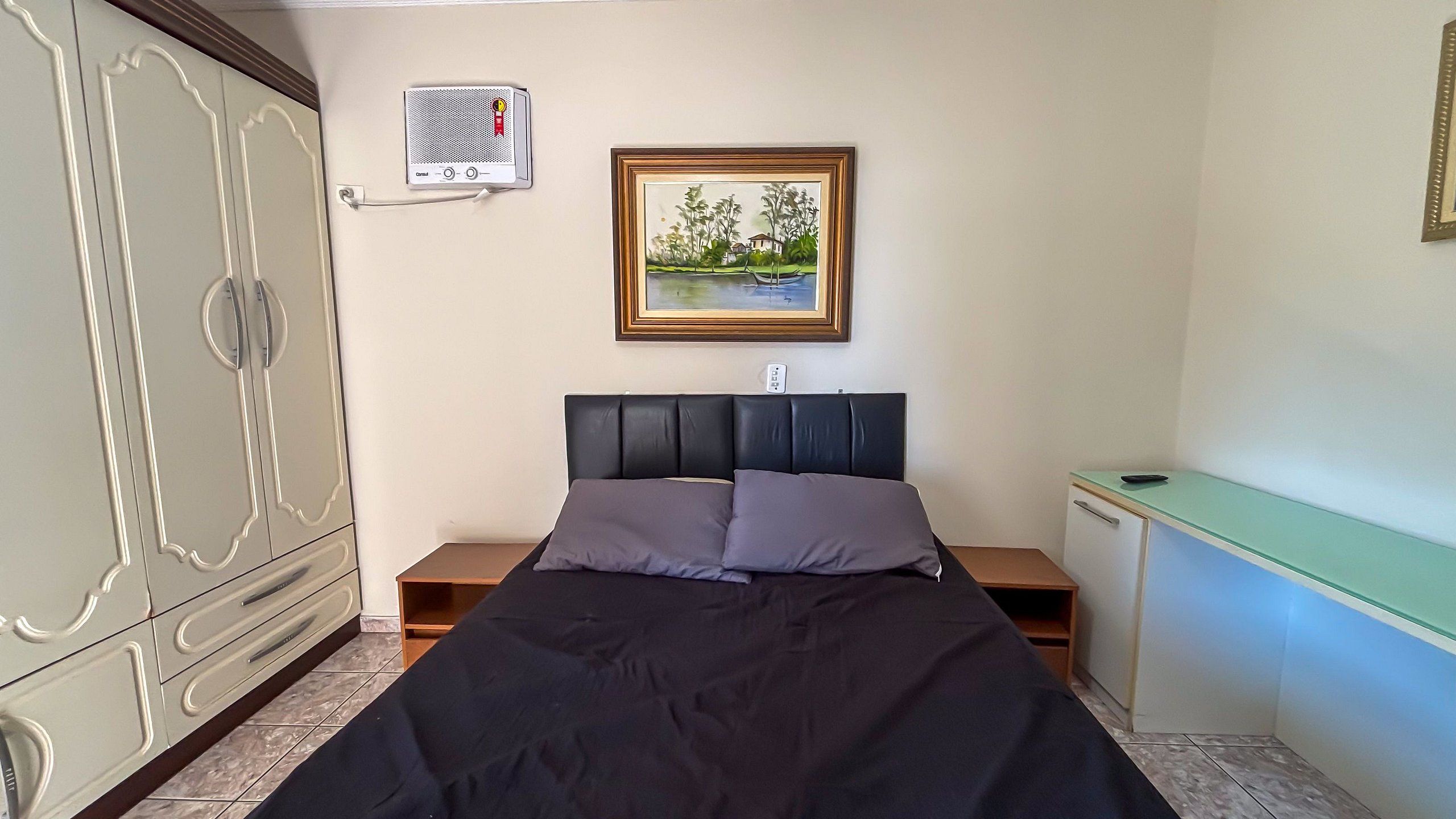 Quarto com cama, mesa de cabeceira, cômoda, escrivaninha e um quadro na parede.