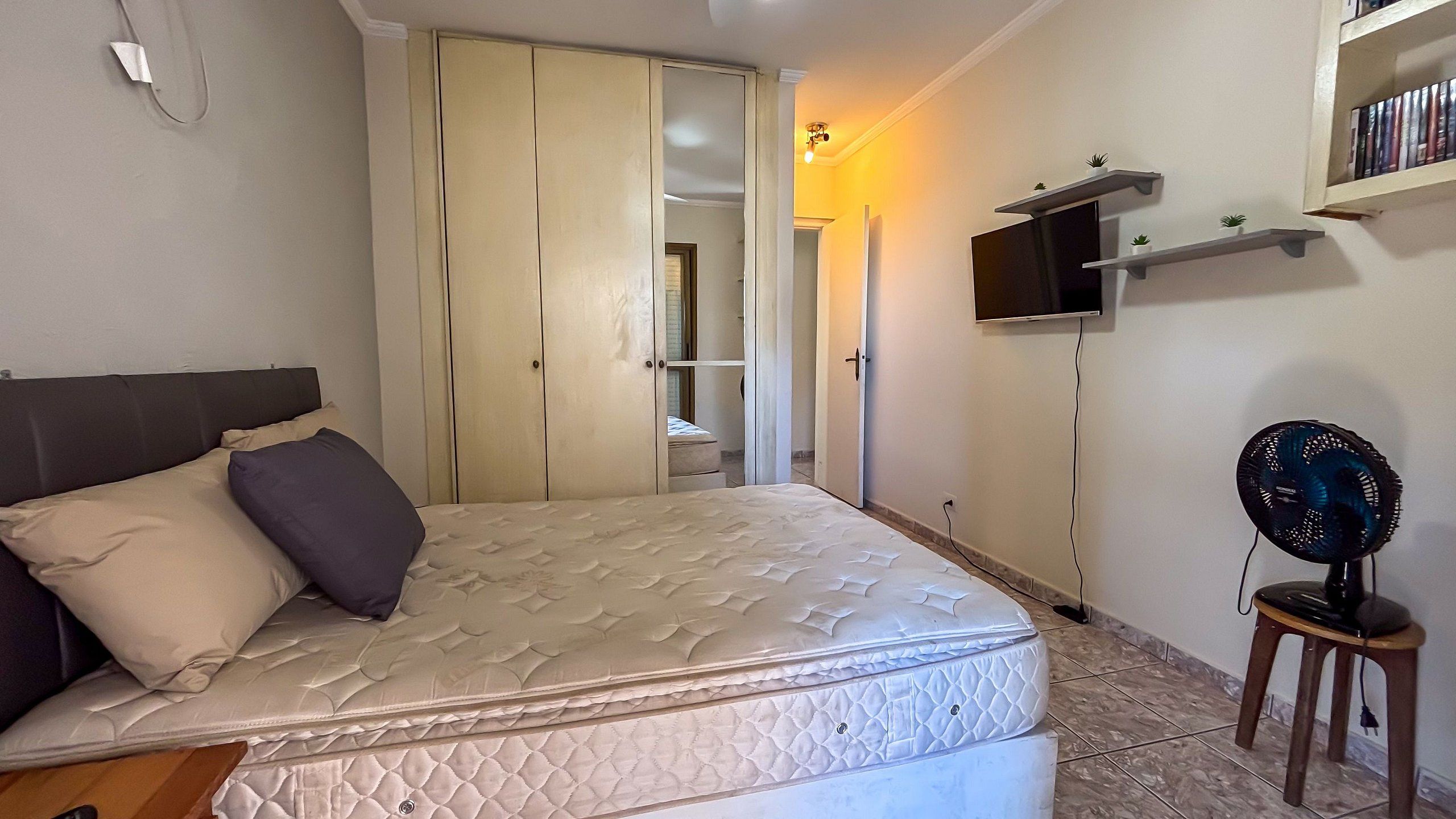 Un dormitorio con cama, televisor, ventilador y armario.