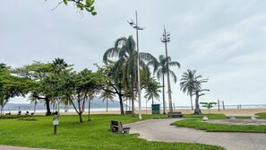 A park with a paved path, benches, and palm trees. - SHB - Churrasco - Piscina - 3 min praia (Guarujá)