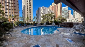 Una piscina en la azotea con sillas de descanso, rodeada de edificios altos.