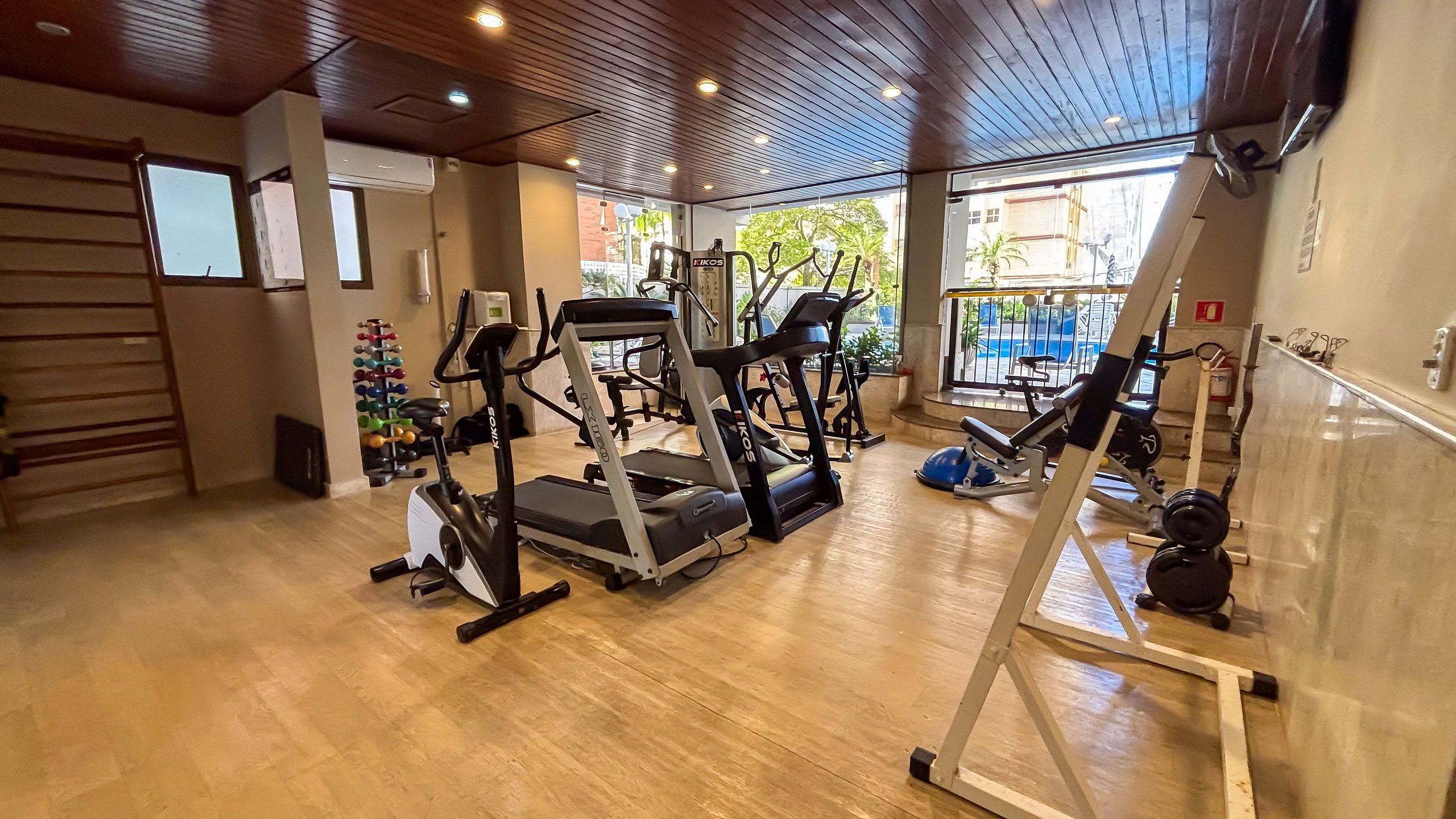 Un gimnasio con cintas de correr, máquinas de pesas y piso de madera.
