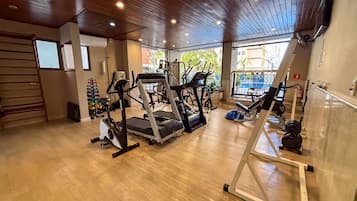 Un gimnasio con cintas de correr, máquinas de pesas y piso de madera.