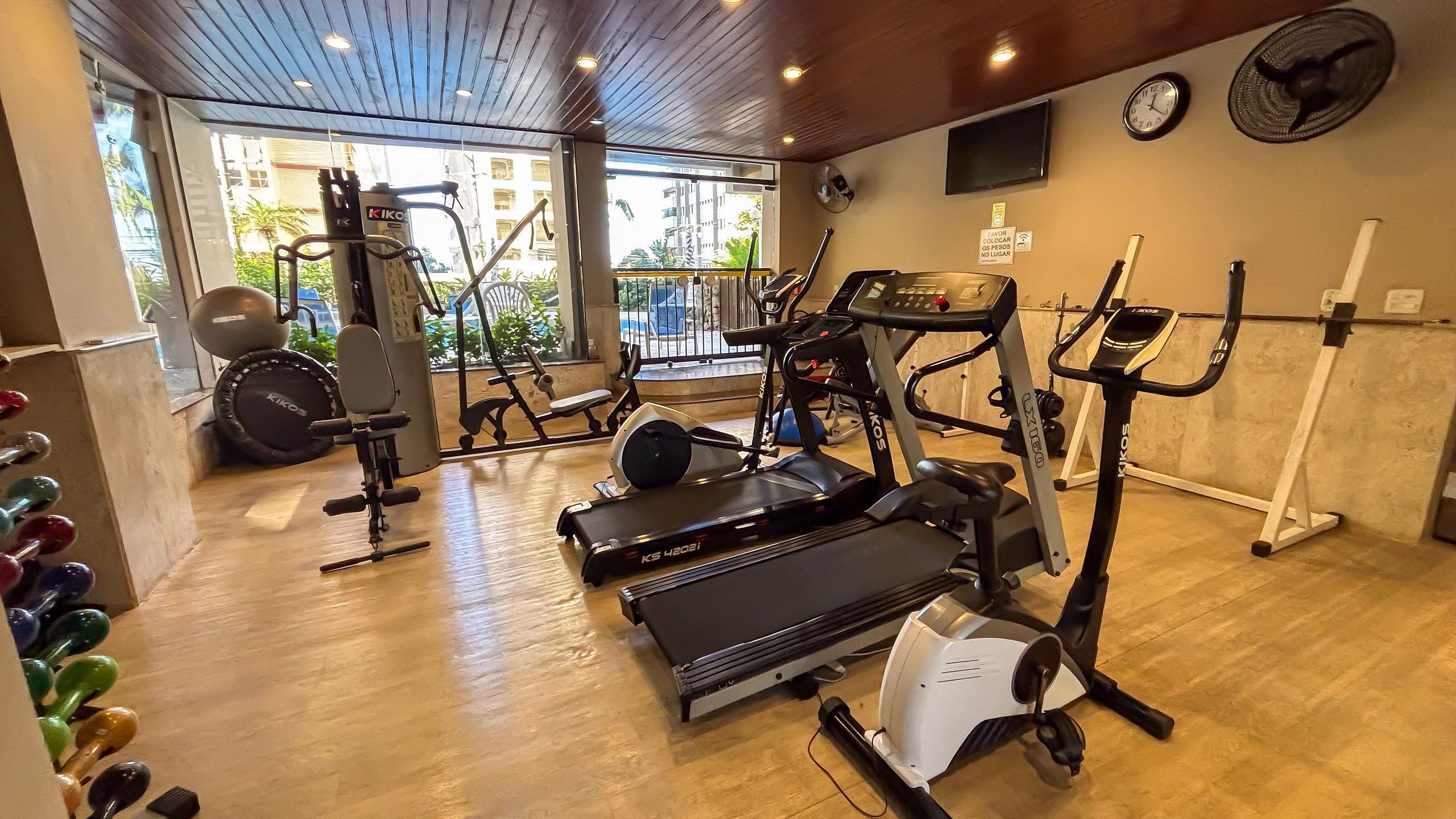 A gym with cardio machines, weight equipment, and a TV on the wall.