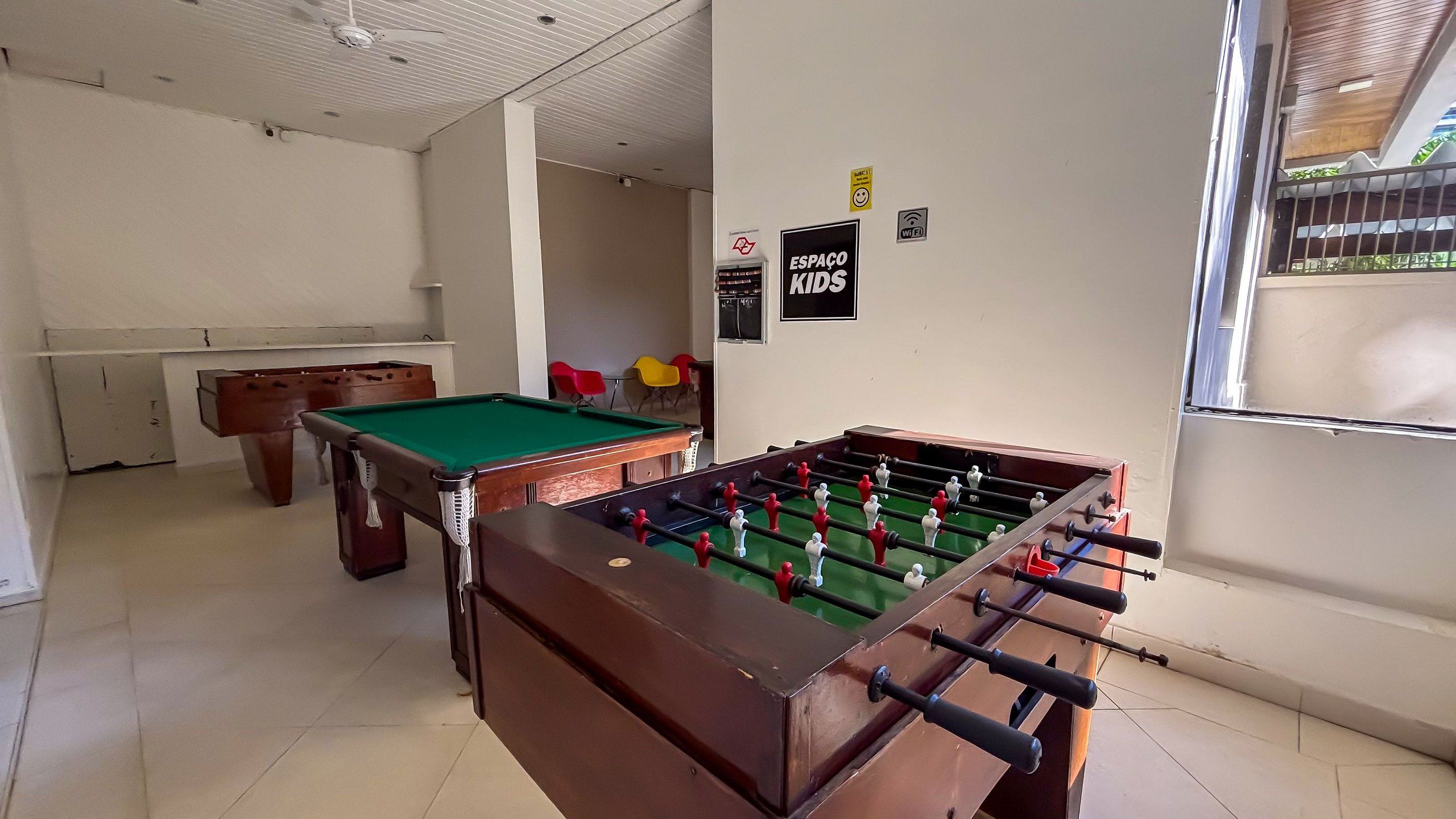 Una mesa de billar, una mesa de fútbol de mesa y una mesa de carambola en una habitación con paredes blancas y suelo de baldosas.