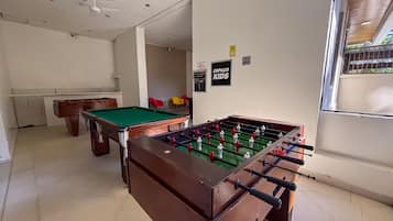 Una mesa de billar, una mesa de fútbol de mesa y una mesa de carambola en una habitación con paredes blancas y suelo de baldosas.