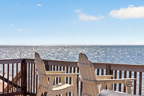 Une terrasse en bois avec deux chaises Adirondack donnant sur une étendue d’eau.