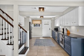A modern kitchen with white cabinets, a blue countertop, and a wooden staircase. - Oceanfront Coastal Escape • Walk to Town • Private Beach (Harwich)