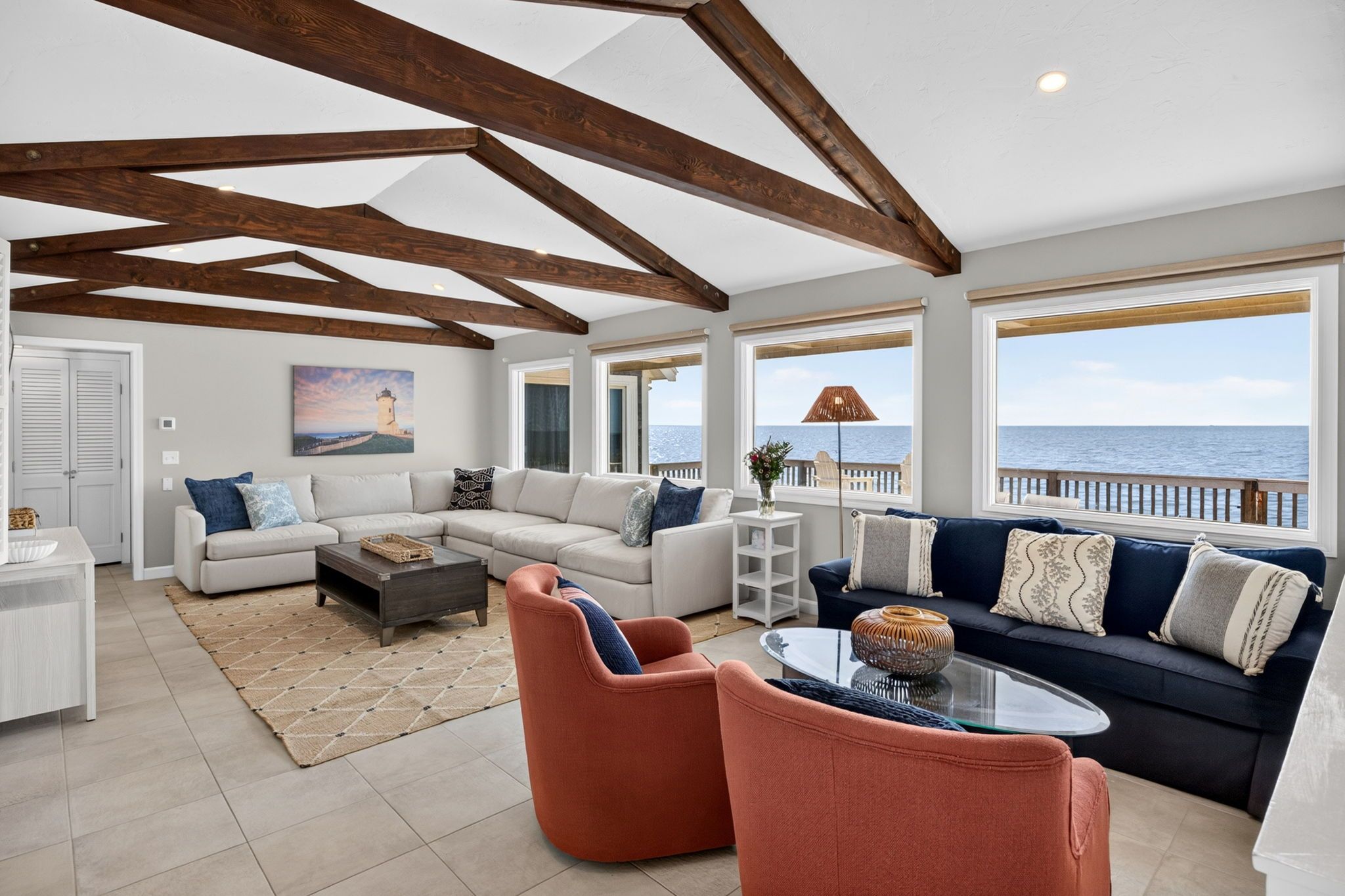 A spacious living area with a large window overlooking the sea, a white sofa, a blue sofa, and a coffee table.