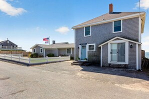 A beachfront property with a two-story house, a white picket fence, and a flag. - Oceanfront Coastal Escape • Walk to Town • Private Beach (Harwich)