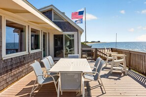 A wooden deck with a table and chairs, overlooking a beach and ocean. - Oceanfront Coastal Escape • Walk to Town • Private Beach (Harwich)