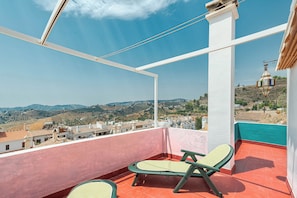 A balcony with two green lounge chairs, a view of a hilly landscape, and a white building with a red roof. - Vistamar Duplex, with spacious terraces and ocean views in Frigiliana (Frigiliana)