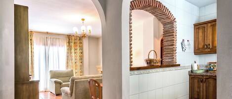 A spacious living area with a sofa and chairs, a kitchen with wooden cabinets, and a tiled floor.