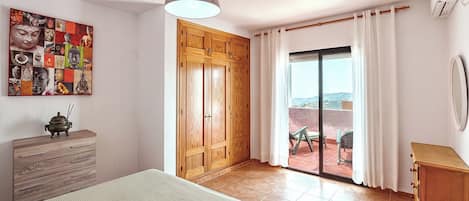 Un dormitorio con cama, un armario de madera, aire acondicionado instalado en la pared y una puerta corredera de cristal que da a un área exterior.