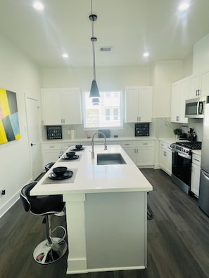 Cozinha moderna com armários brancos, uma ilha central e luminária pendente preta.