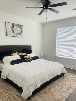 A bedroom with a bed, a ceiling fan, a window with blinds, and a wall-mounted artwork. - Luxury Living Collection 
Black & White Edition (Houston)