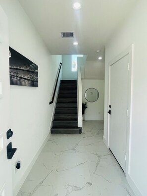A hallway with a staircase, a door, and a wall-mounted light fixture. - Luxury Living Collection 
Black & White Edition (Houston)
