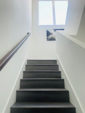 Eine Treppe mit dunklen Stufen, die nach oben führen, einer Geländer links und einem Fenster oben.