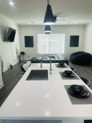 A modern kitchen with a central island, a built-in sink, and a black pendant light. - Luxury Living Collection 
Black & White Edition (Houston)