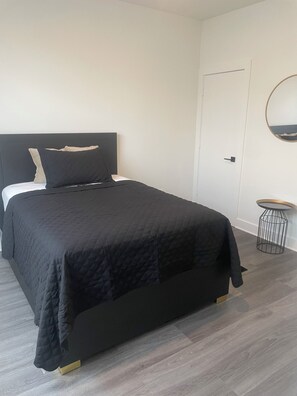 Ein Schlafzimmer mit einem Bett, einem Nachttisch, einem runden Spiegel und einer Tür.