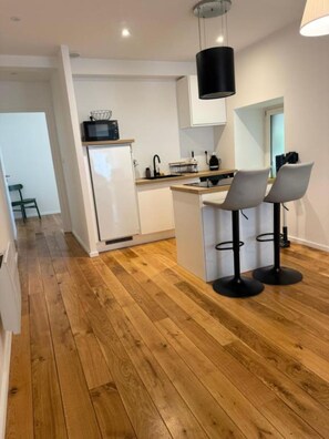 A modern kitchen with a central island, bar stools, and a wooden floor. - Cozy, fully equipped one-bedroom apartment in the city center (Brest)