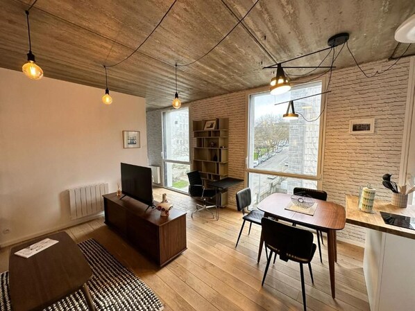 A modern living space with a wooden floor, a sofa, a TV, a dining table with chairs, and a kitchen area. - Cozy, fully equipped one-bedroom apartment in the city center (Brest)