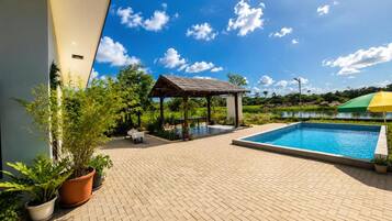 A pool area with a gazebo, potted plants, and a view of a lake.