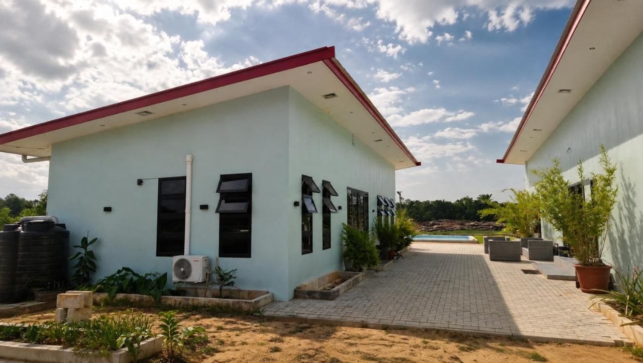 Um edifício de dois andares com telhado vermelho, um caminho pavimentado e uma piscina ao fundo.