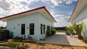 A two-story building with a red roof, a paved walkway, and a swimming pool in the background. - Guesthouse AngaLampoe (Lelydorp)