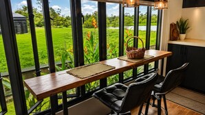 A dining area with a view of a green landscape through large windows. - Guesthouse AngaLampoe (Lelydorp)