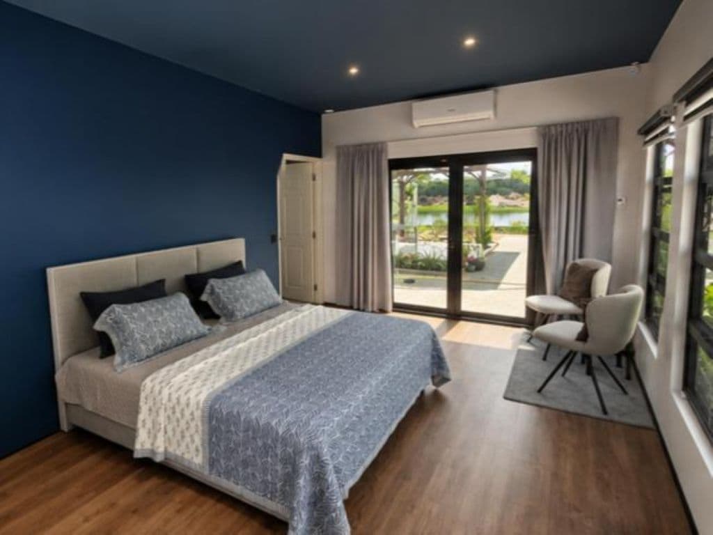 Quarto com cama, uma cadeira e vista para área externa.
