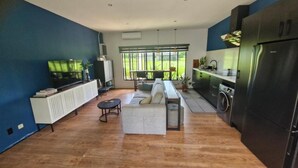 A modern kitchen with a built-in oven, a dining area with a bench, and a large window offering a view of greenery. - Guesthouse AngaLampoe (Lelydorp)
