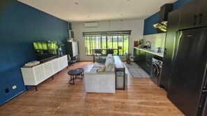 A modern kitchen with a built-in oven, a dining area with a bench, and a large window offering a view of greenery. - Guesthouse AngaLampoe (Lelydorp)