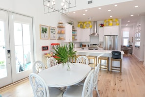 A modern kitchen with white cabinetry, a central island, and a dining area with white chairs. - Most Kid-Friendly 30A Home + Private Heated Pool + Golf Cart + All Beach Gear (Inlet Beach)