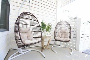 Zwei hängende Korbstühle mit Kissen, ein kleiner Holztisch und ein Blumentopf auf einer Veranda.