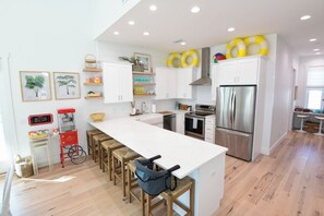 A modern kitchen with white cabinetry, a stainless steel refrigerator, and a bar area with stools. - Most Kid-Friendly 30A Home + Private Heated Pool + Golf Cart + All Beach Gear (Inlet Beach)